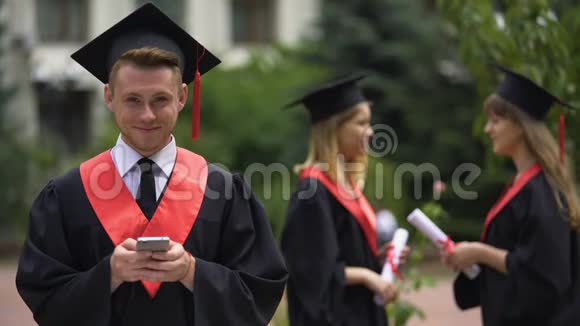 年轻的男毕业生拿着智能手机微笑着拍照毕业典礼视频的预览图