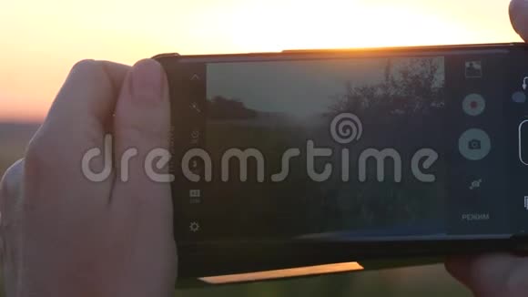 剪影手提智能手机在日落和耀斑灯光下拍照视频的预览图