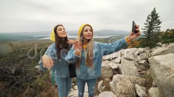 两个年轻快乐的女人在美丽的山顶上跳舞举起手臂越过夕阳的天空视频的预览图