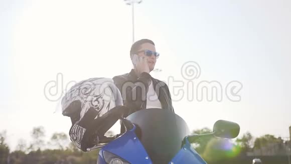 一个穿着皮夹克和太阳镜坐在摩托车上玩电话的年轻人视频的预览图