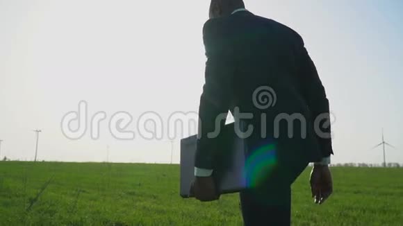 一个穿着商务服的黑人手里拿着一台笔记本电脑走在一片绿色的草地上慢动作视频的预览图