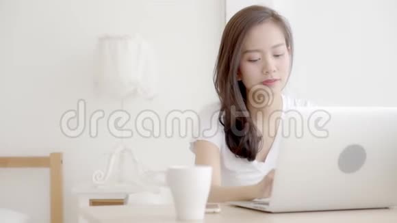 美丽的年轻自由职业亚洲女性微笑着工作在笔记本电脑和手机上聊天视频的预览图