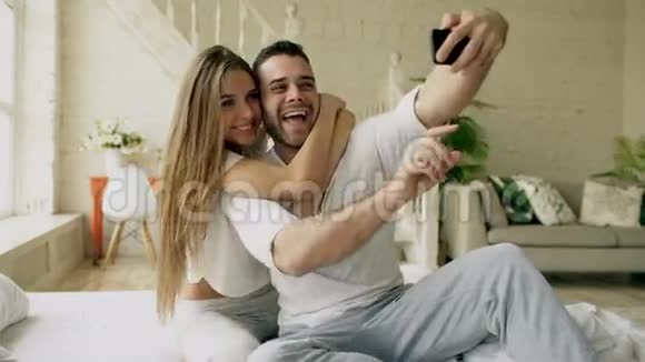 年轻美丽可爱的一对情侣在智能手机上拍照早上坐在床上接吻视频的预览图
