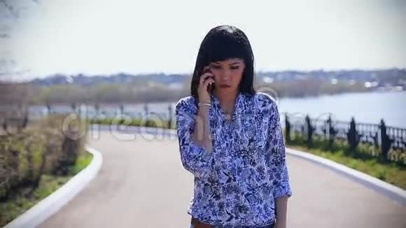 美丽的亚洲女孩穿着牛仔裤在阳光明媚的一天在公园里散步打电话视频的预览图