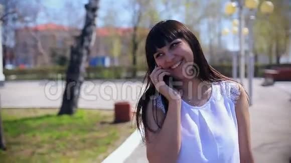穿着白色衬衫的东方美女微笑着在公园里散步打电话视频的预览图