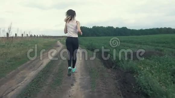 快乐的运动女孩在田间的道路上奔跑户外健身用安定剂射击视频的预览图