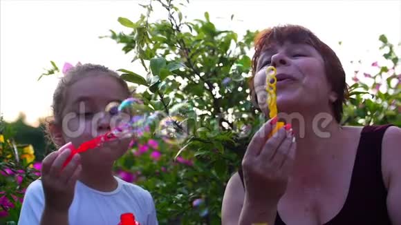 幸福微笑的家人奶奶带着孙女正在玩耍在夏天的户外吹肥皂泡股票股票视频的预览图