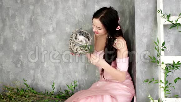 年轻的女士在照相馆里摆姿势手里拿着小白兔手里拿着柳条灰色篮子女孩玩得很开心视频的预览图