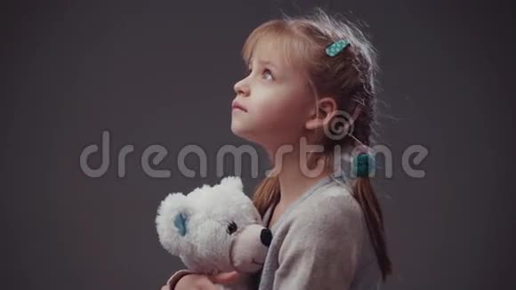 可爱的欧洲女孩有两条辫子和蓝色悲伤的大眼睛穿着时尚的米色毛衣孩子拿着她最喜欢的玩具视频的预览图