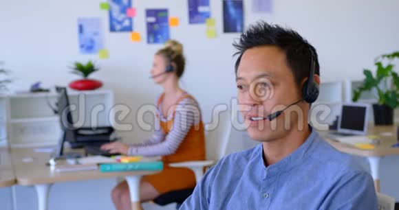 年轻的亚洲男性高管在办公桌旁的耳机上交谈视频的预览图
