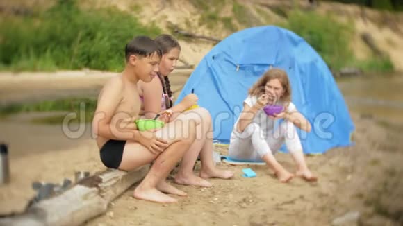 一位妇女和她的孩子们正在一个营地的水壶附近吃一顿饭背景是一个帐篷视频的预览图