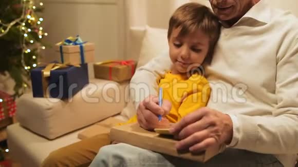 可爱的小男孩和他的祖父在圣诞礼物上签名视频的预览图