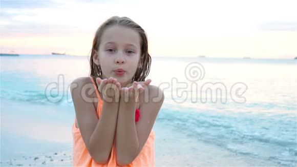 海滩上可爱的小女孩在日落时玩得很开心快乐的孩子看着镜头和亲吻的背景视频的预览图