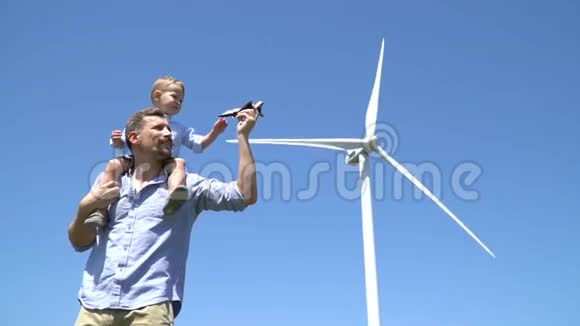 父亲把儿子扛在肩上和他玩对着风力发电机的背景射击视频的预览图