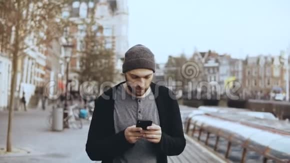 4K高加索游客带着智能手机走路休闲英俊的胡须微笑的成年男性在街上发短信视频的预览图