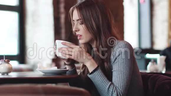年轻迷人的女孩坐在舒适的咖啡馆里用手机视频的预览图