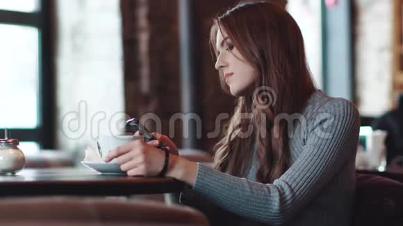 年轻迷人的女孩坐在舒适的咖啡馆里用手机视频的预览图