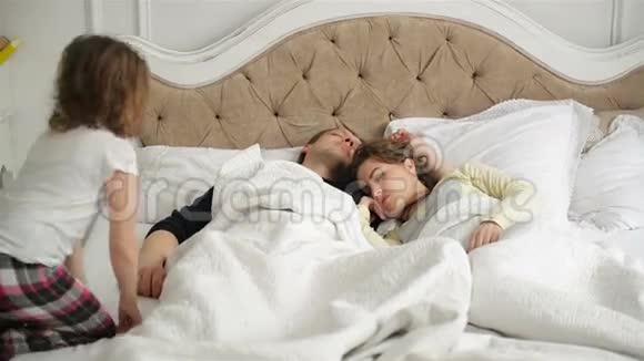 年轻夫妇正在家中睡在床上活跃的小女孩正在唤醒她熟睡的父母视频的预览图