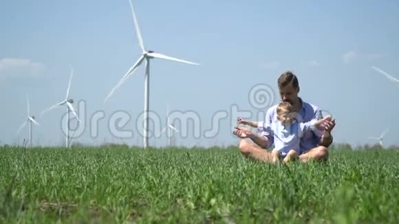 爸爸和儿子坐在草地上躺在风力发电机的背景上视频的预览图
