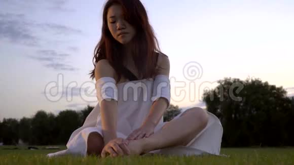体贴的日本女孩穿着白色连衣裙抓住她的腿坐在草地上视频的预览图