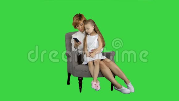 可爱的小女孩坐在妈妈的膝盖上一边用绿色屏幕上的手机说话Chroma键视频的预览图