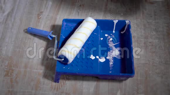 油漆滚筒躺在地板上的蓝色托盘里是一种扁平的白色染料从水桶工具和材料中流出视频的预览图