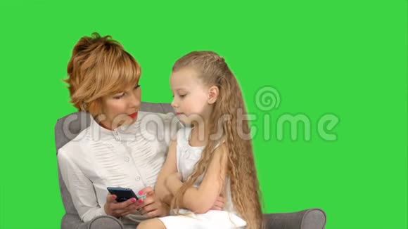 年轻女子母亲和孩子在绿色屏幕上看电话彩色钥匙视频的预览图