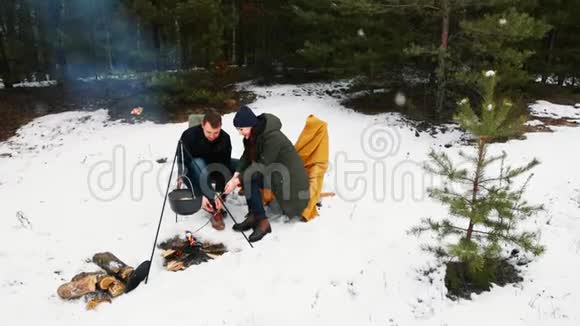 这对夫妇坐在冬天森林里的篝火旁坐在舒适的沙发上下雪了冬季快乐概念视频的预览图