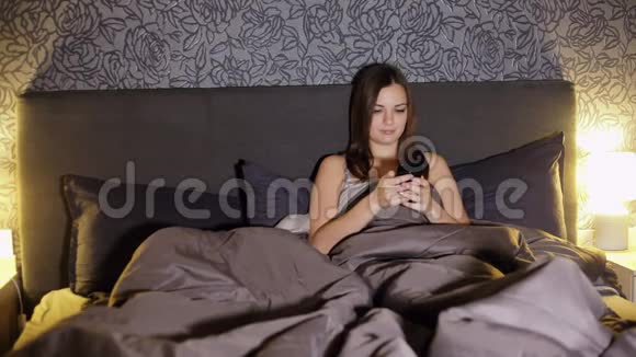 年轻女子晚上躺在卧室的床上上网视频的预览图
