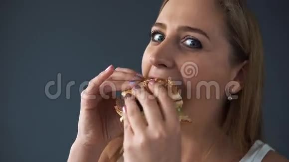 超重的女人吃汉堡包看着灰色背景的相机特写镜头有害食品的概念视频的预览图