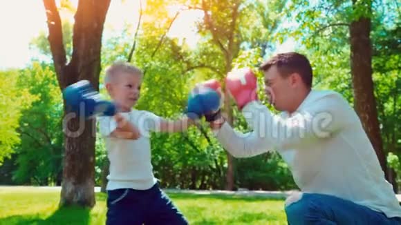 父亲和儿子戴着拳击手套在房子附近的草坪上打拳击视频的预览图