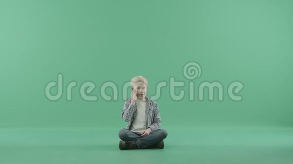 男孩坐在地板上在绿色背景下有感情地打电话视频的预览图