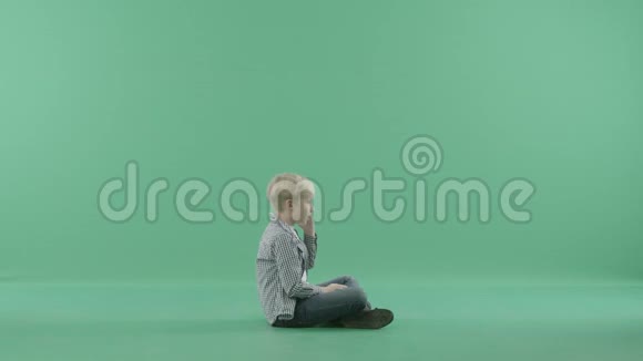 孩子侧着身子坐着在绿色背景下打电话视频的预览图