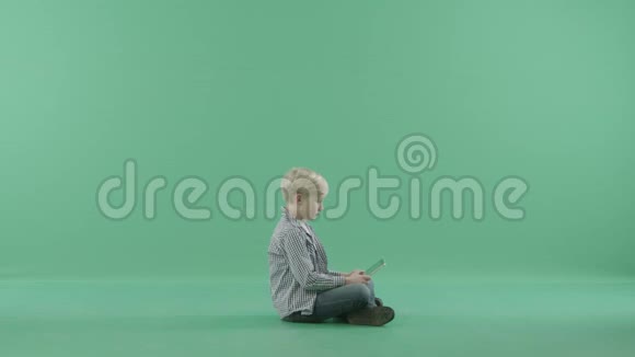 微笑的男孩侧着身子坐在地板上用他的战术平板电脑视频的预览图