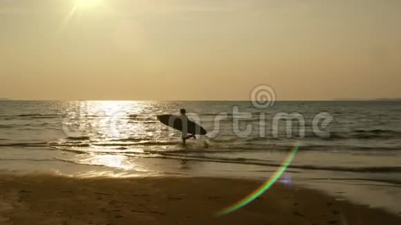 在热带海滩日落时年轻快乐的冲浪带着长长的冲浪板奔跑的剪影海边的冲浪者视频的预览图