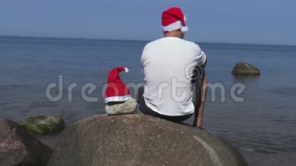 在海边的石头上戴着圣诞老人帽子的人视频的预览图