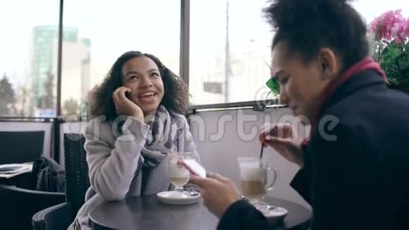 性感混血女人坐在街边咖啡馆的桌子旁一边说着手机一边她的朋友在冲浪视频的预览图