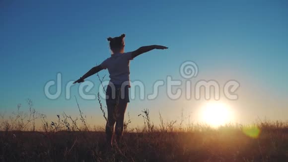 剪影小女孩挥手在草地上与日落日落时分在田野里快乐的漂亮女孩视频的预览图