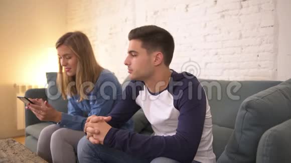 在手机上使用社交媒体对年轻女性进行恐吓无视男友在家沙发沙发上的举动而这位男性则感到沮丧视频的预览图