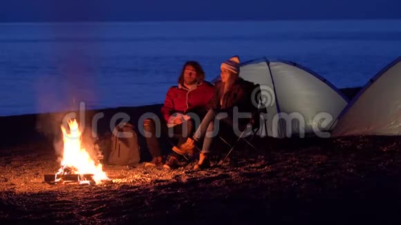 一对年轻夫妇坐在火炉旁在海边用帐篷露营春晚视频的预览图