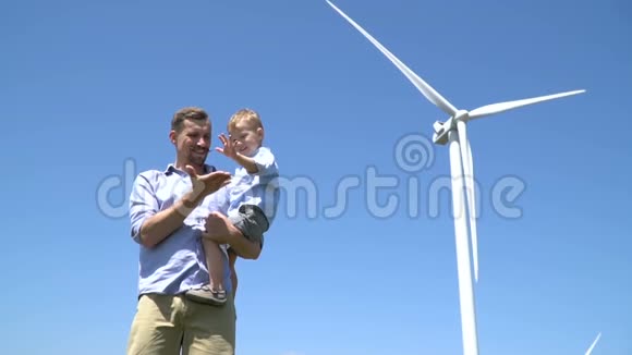 父亲挽着儿子的胳膊在蓝天的风力发电机的背景下和他玩耍视频的预览图