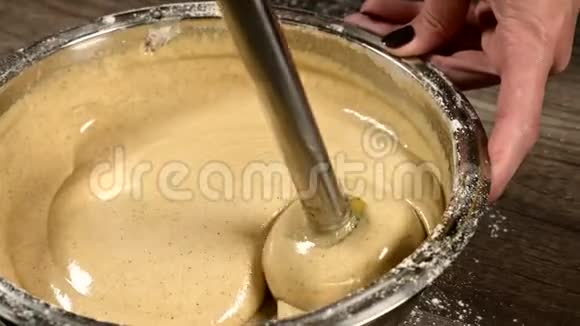 厨房里的一个糕点女孩在一个金属碗里特写用搅拌机敲打面团做海绵蛋糕家庭烹饪视频的预览图