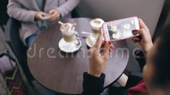 坐在户外的街头咖啡馆里用智能手机近距离拍摄咖啡杯视频的预览图