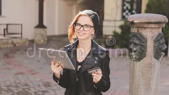 年轻的现代时尚女孩通过互联网支付订单使用一张银行卡和平板电脑坐在院子里视频的预览图