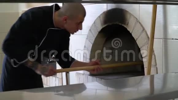 一个年轻的披萨师傅在餐馆的厨房里做披萨厨师把比萨饼放在热烤箱里然后把它翻过来视频的预览图