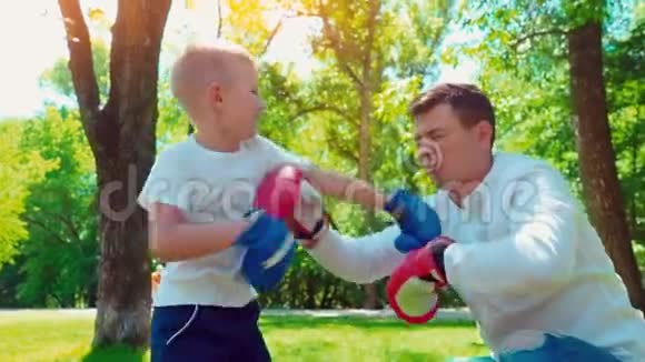 父亲和儿子戴着拳击手套在房子附近的草坪上打拳击视频的预览图