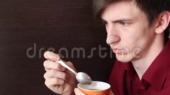 一个年轻人拿出一勺茶在杯子的边缘用嘴舔它视频的预览图