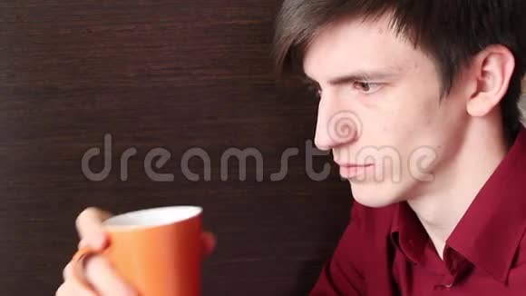 一个年轻人喝着橙色的杯子总是看着视频的预览图