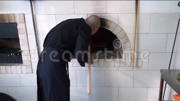 一个年轻的披萨师傅在餐馆的厨房里做披萨厨师把比萨饼放在热烤箱里然后把它翻过来视频的预览图