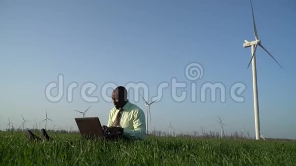 身穿西装的黑人坐在绿色草地上喜欢笔记本电脑上的机器人视频的预览图